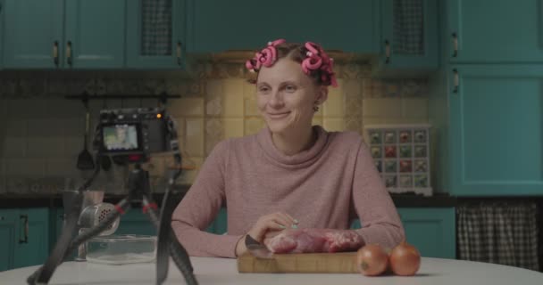 여성 블로거가 부엌에 앉아 있는 카메라로 요리하고 녹화하는 영상을 보고 있습니다. 머리에 곱슬머리를 하고 집에서 요리를 하고 vlog 를 녹음하는 주부. — 비디오