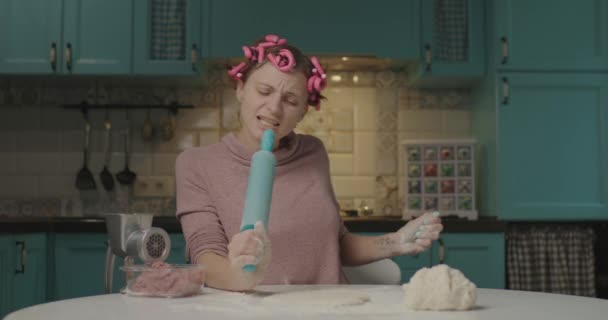 Jeune femme adulte heureuse déroulant la pâte et chantant dans le micro à rouleau assis dans la cuisine. Femme au foyer drôle avec boucleur de cheveux cuisine à la maison seule. — Video