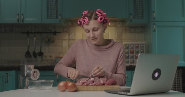 Fiatal nevető nő főz és beszél online barátaival. Nő vágás hús és beszélgetés barátaival laptopon, mert a társadalmi távolság. — Stock videók