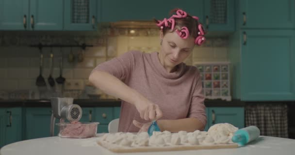 Jonge volwassen vrouw die deegcirkels maakt voor dumplings in de keuken. Huisvrouw met haarkrultang die alleen thuis kookt. Zelfgemaakte knoedels op het bord. — Stockvideo