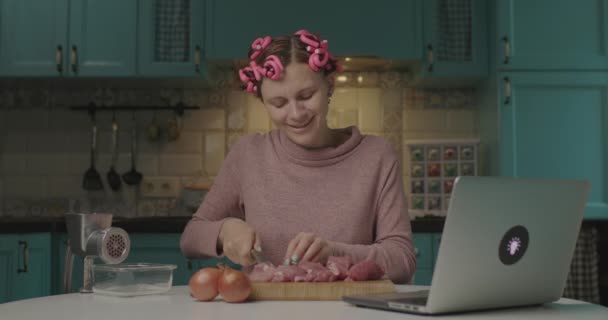 Młoda dorosła kobieta gotowanie i śmiech podczas rozmowy online z przyjacielem. Kobieta kroi mięso i rozmawia z przyjaciółmi przez laptopa ze względu na odległość społeczną. — Wideo stockowe