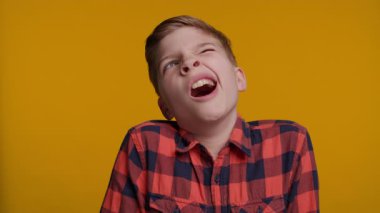 Genç bir çocuk esniyor, uykusuzluk ya da can sıkıntısı belirtileri gösteriyor. Parlak sarı arka plan yorgun ifadesini ve doğal tepkisini vurguluyor..