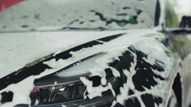 Bir araba, bir oto yıkama istasyonunda tamamen kalın, beyaz köpükle kaplıdır, parlak bir bitiş için temizlik ve detay sürecini vurgular..