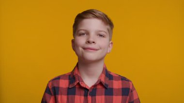 Genç bir çocuk kameraya sıcak bir şekilde gülümsüyor, tatmin olmuş ve mutlu bir ifade sergiliyor. Parlak sarı arka plan, sahneye neşeli ve olumlu bir hava katar..