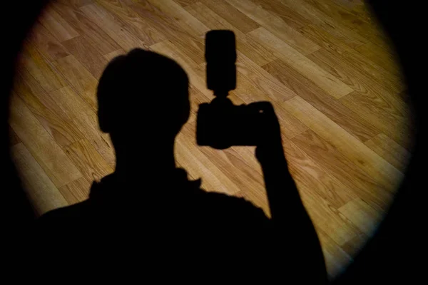 silhouette of a man with a camera in the beam of light on the parquet floor