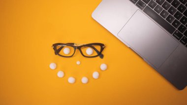 Boş parlak sarı arka plan üzerinde iş yeri masası, gözlük ve gülen yüz ile dizüstü bilgisayar üst görünümü