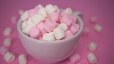 Işıl ışıl pembe arka planda leziz şekerleme dolu beyaz bir fincan.