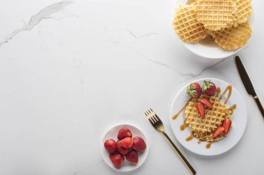 altın çatal ve bıçak ile beyaz bir arka plan üzerinde beyaz bir tabak üzerinde çilek ile waffle