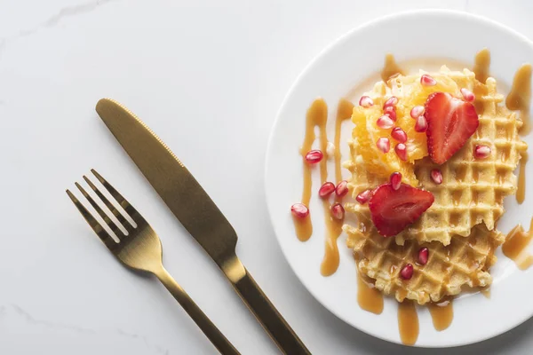 altın çatal ve bıçak ile beyaz bir arka plan üzerinde beyaz bir tabak üzerinde çilek ile waffle