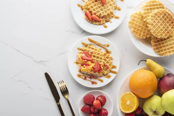 altın çatal ve bıçak ile beyaz bir arka plan üzerinde beyaz bir tabak üzerinde çilek ile waffle