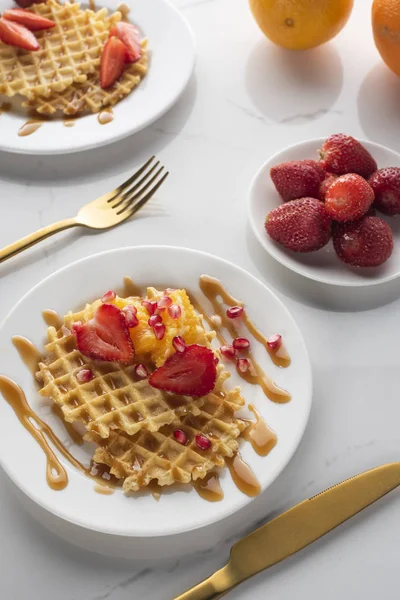 altın çatal ve bıçak ile beyaz bir arka plan üzerinde beyaz bir tabak üzerinde çilek ile waffle