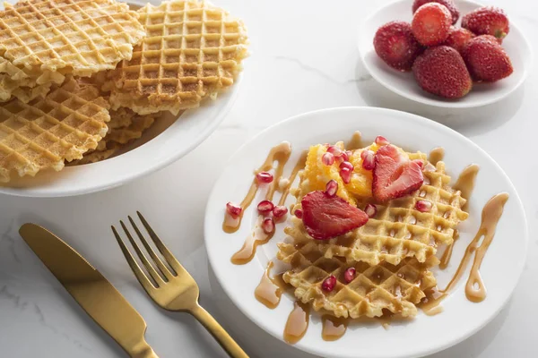 altın çatal ve bıçak ile beyaz bir arka plan üzerinde beyaz bir tabak üzerinde çilek ile waffle