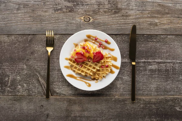 altın çatal ve bıçak ile beyaz bir arka plan üzerinde beyaz bir tabak üzerinde çilek ile waffle