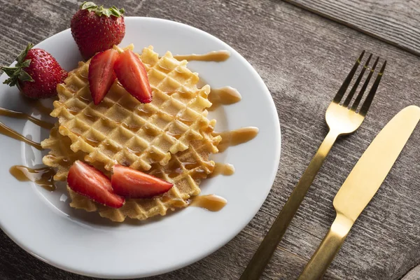 altın çatal ve bıçak ile beyaz bir arka plan üzerinde beyaz bir tabak üzerinde çilek ile waffle