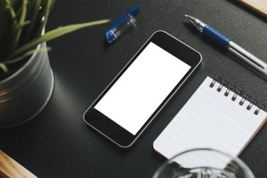Smartphone ekran yukarı sahte çapraz görünümünü bir defter, kalem, bir bardak su ve yeşil bir bitki ile siyah bir tabloda.