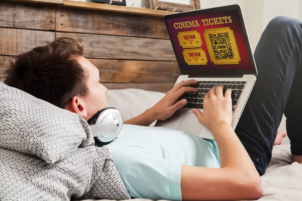 男子购买在线电影院门票在互联网上与笔记本电脑 而躺在床上在家 — 图库照片