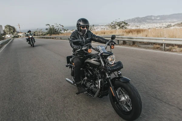 Man in black clothes riding a black classic american motorcycle