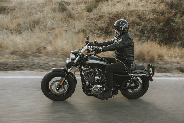 Man in black clothes riding a black classic american motorcycle 