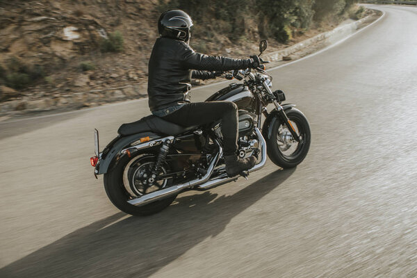 Side view of classic motorbike rider turning in a road with an American classic motorcycle