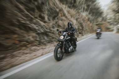 Bir motosiklet sürme yolda dağ arasında siyah deri ceketli adamı.