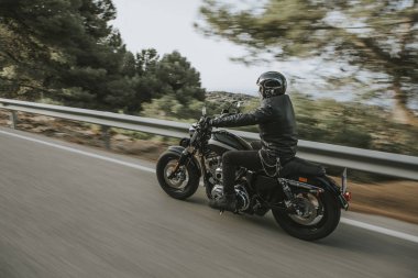 Bir motosiklet sürme yolda dağ arasında siyah deri ceketli adamı.