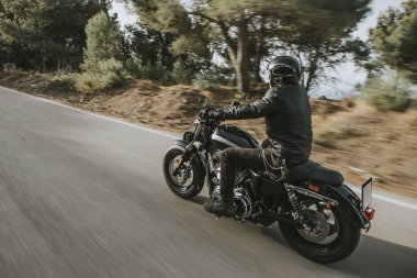 Bir motosiklet sürme yolda dağ arasında siyah deri ceketli adamı.