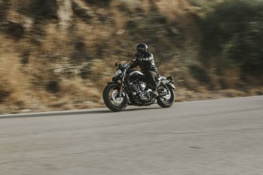 Bir motosiklet sürme yolda dağ arasında siyah deri ceketli adamı.