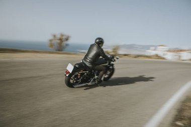 Adam arka plan mavi gökyüzünde olan dağ, yol içinde hızlı bir Amerikan motosiklet Binme siyah giysili. Arkadan görünüm.