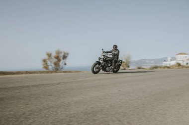 Adam arka plan mavi gökyüzünde olan dağ, yol içinde hızlı bir Amerikan motosiklet Binme siyah giysili.