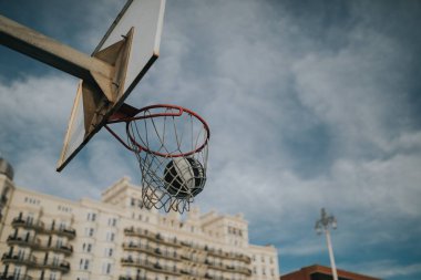 BRIGHTON, ENGLAND - October 24th, 2018: Spalding Ball entering into basketball basket ring in a street  basketball court, with blue sky in the background, at sunset. clipart