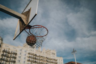 BRIGHTON, ENGLAND - October 24th, 2018: Spalding Ball entering into basketball basket ring in a street  basketball court, with blue sky in the background, at sunset. clipart