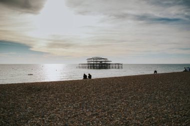 Arka planda Brighton West Pier Brighton beach sahne eski ile yanmış ve denizin üzerinde oturan insanlar shore.