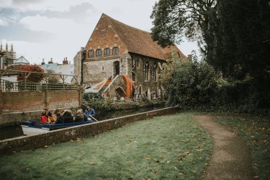 Canterbury, İngiltere - 28 Ekim 2018: Canterbury, İngiltere'de arka planda bir kilise ile Stour Nehri boyunca küçük bir tekne içinde turistik bir seyahat zevk insanlar.