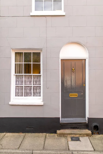 Typical english house facade with grey door and white window viewed from outdoors.