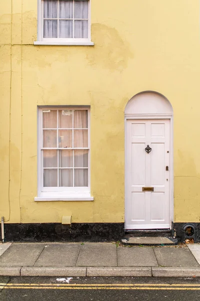 Yellow and white typical english house facade with door and window viewed from outdoors.