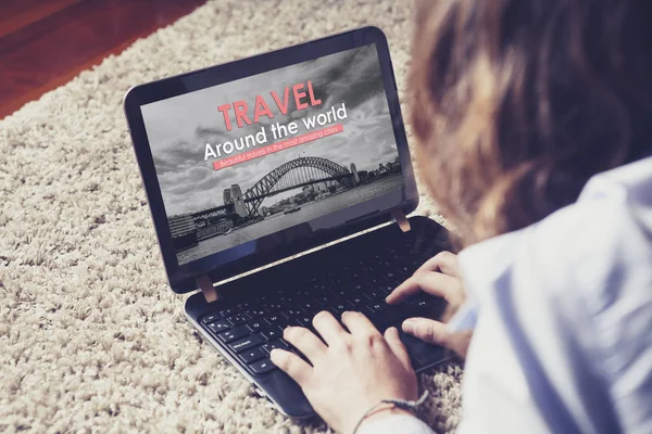 Travel agency website in a laptop screen while woman uses it to book a travel at home.