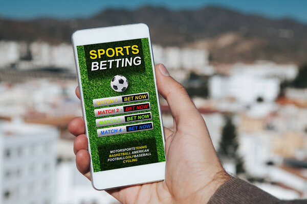 Man holding a mobile phone in the hand with sports betting website in the screen, with city background.