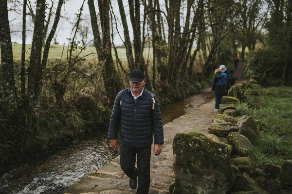 Camino de Santiago yolunda yürüyüş adam, nehir tarafından bir taş köprü geçerek.