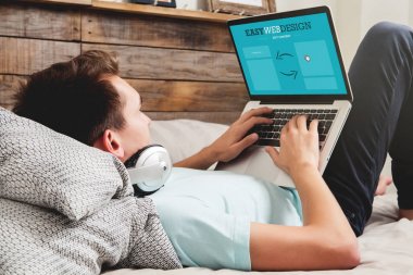 Evde yatakta yatarken bir dizüstü bilgisayar ile web tasarımı yapma Adam.