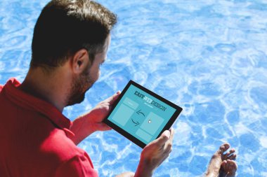 Yüzme havuzu kıyısında otururken ekranda web tasarım uygulaması ile bir tablet tutan adam.