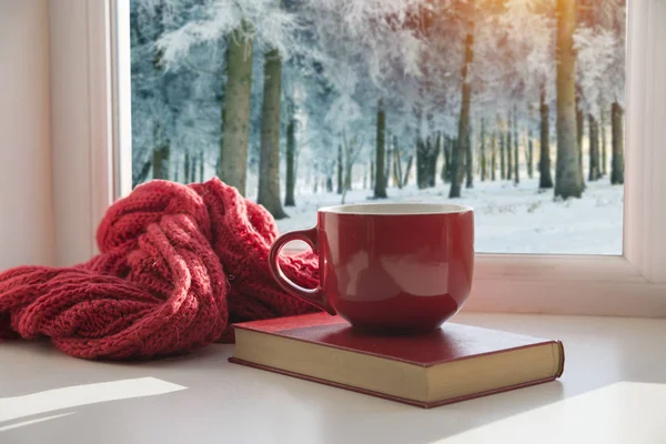 Чашка горячего кофе и уютный вязаный шарф на деревянном столе перед блестящим фоном со снежинками — стоковое фото