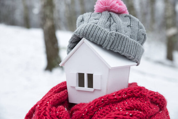 дом зимой - концепция системы отопления и холодная снежная погода с моделью дома в вязаной шапке
