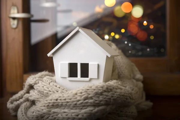 Casa no inverno - conceito de sistema de aquecimento e tempo nevado frio com modelo de uma casa usando um boné de malha — Fotografia de Stock