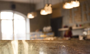 Kafenin soyut bulanık arka planının önündeki boş ahşap masa. Ürünlerinizi görüntülemek veya montajlamak için kullanılabilir. Ürünün görüntülenmesi için modelleyin