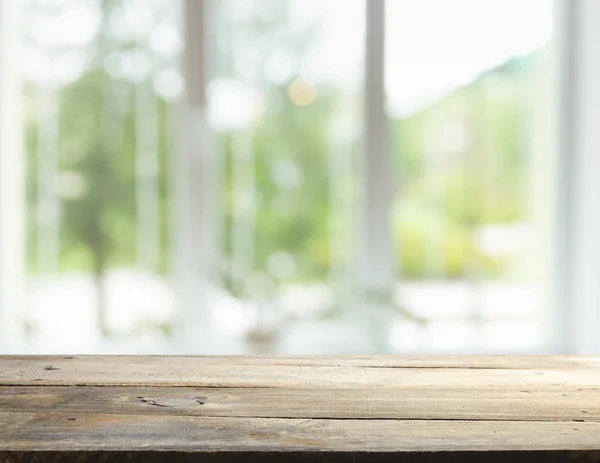 Mesa de madera en desenfoque de cristal de la ventana y verde abstracto del jardín con vista a la ciudad en el fondo de la mañana. Para la exhibición del producto de montaje —  Fotos de Stock