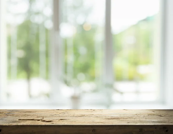 Mesa de madera en desenfoque de cristal de la ventana y verde abstracto del jardín con vista a la ciudad en el fondo de la mañana. Para la exhibición del producto de montaje —  Fotos de Stock