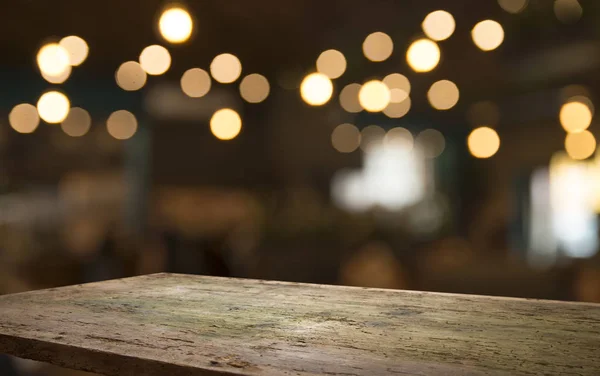 Prázdný dřevěný stůl nahoře na světle vyostřené zlaté bokeh Café Restaurant na tmavém pozadí — Stock fotografie