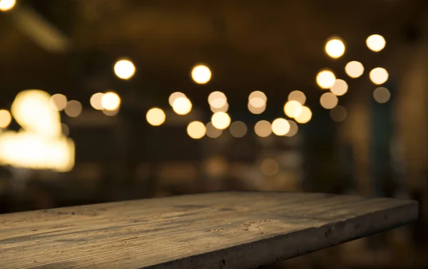 Prázdný dřevěný stůl nahoře na světle vyostřené zlaté bokeh Café Restaurant na tmavém pozadí — Stock fotografie