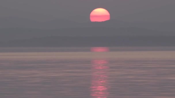 Zeitraffer der untergehenden Sonne über den Bergen. Reflexion im Wasser. große Sonnenscheibe — Stockvideo