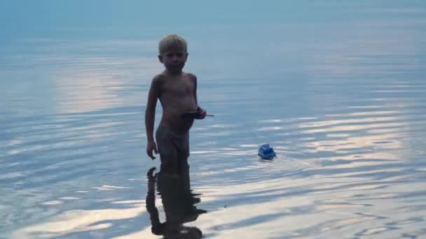 6 éves fiú elindít egy hajót, miközben a vízben áll. — Stock videók